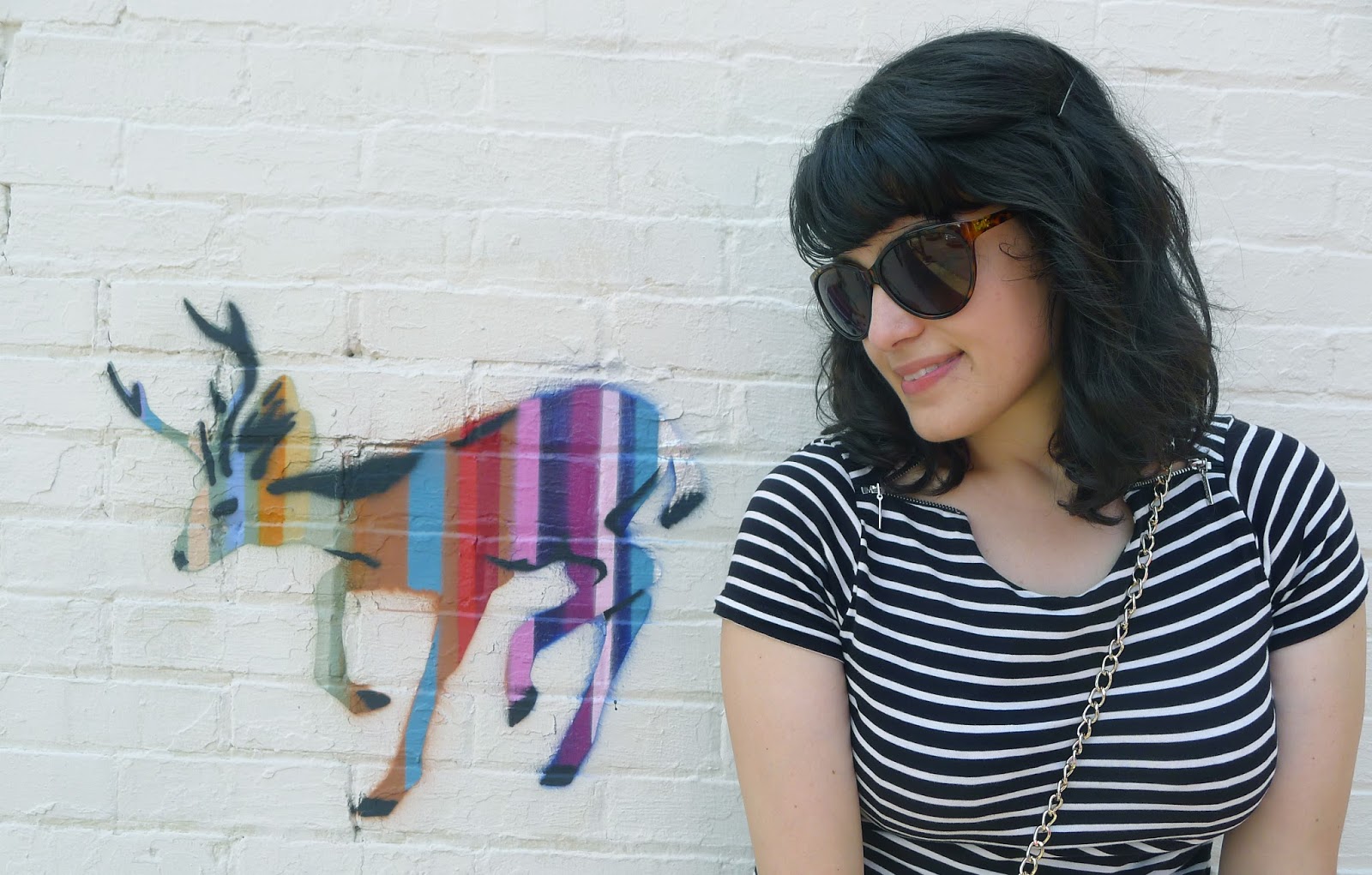 Tracie's headshot taken against a white brick wall painted with a rainbow-striped deer.